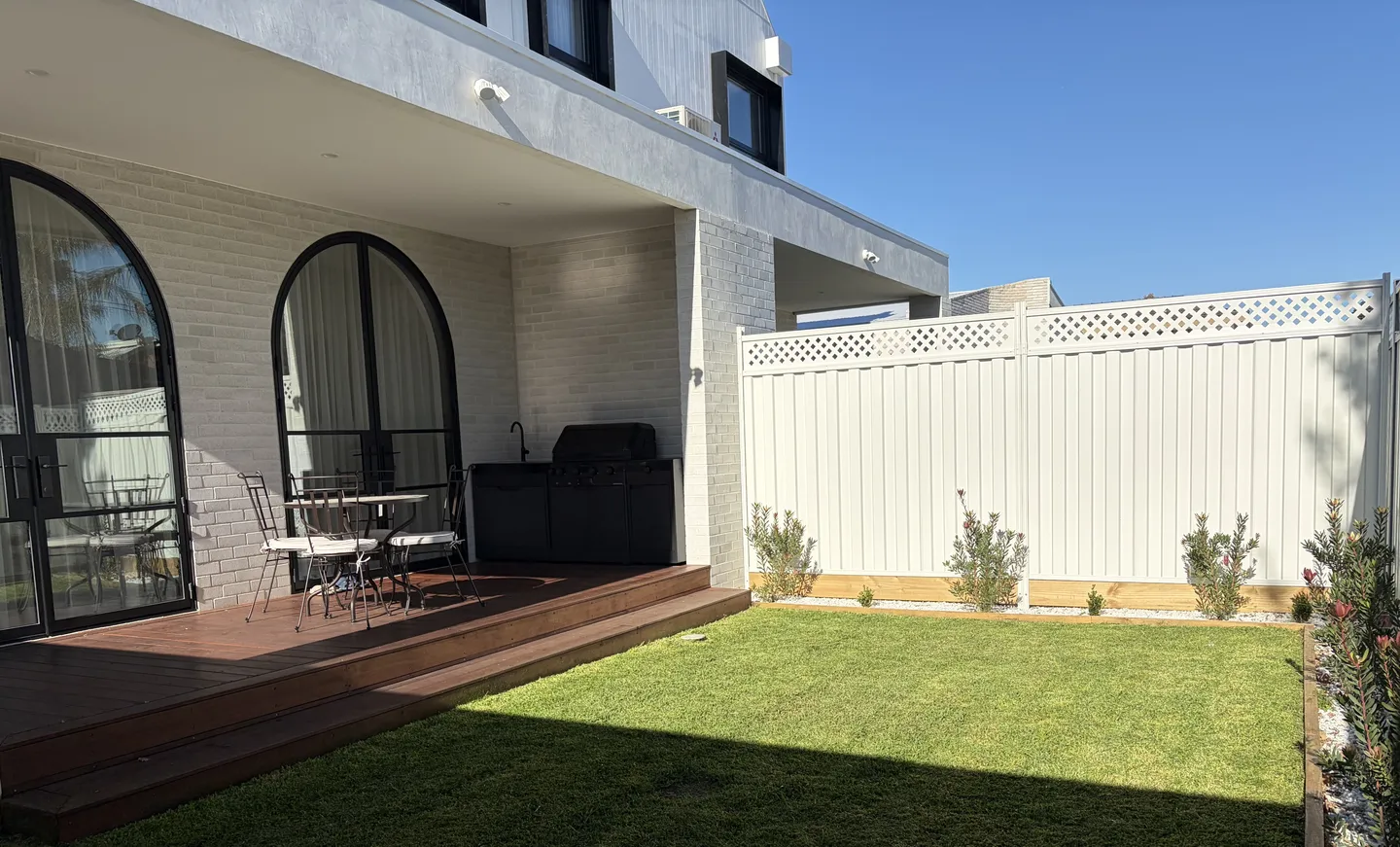 A modern residential backyard featuring a freshly mown green lawn next to a timber deck patio